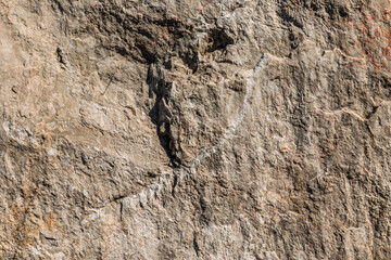 primo piano di una superficie di pietra ruvida e con tanti piccoli rilievi, dalle sfumature di colore grigio, illuminata frontalmente dal sole