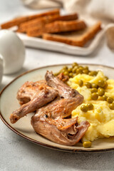 Pieces of rabbit stew, mashed potatoes and green peas on a plate on a bright table closeup