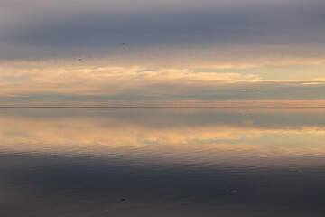 dettagli del cielo nuvoloso, colorato parzialmente di arancione leggero dalla luce del sole al tramonto che si riflette sul mare Adriatico piatto e calmo con effetto specchio