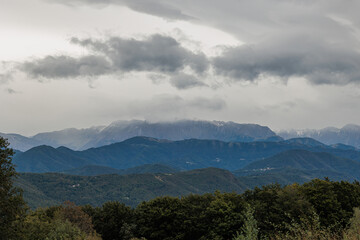 vista su varie colline e montagne nella Slovenia occidentale, di pomeriggio, a inizio autunno, con il cielo coperto completamente da grandi nuvole grigie 