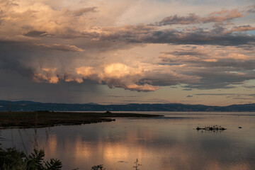 temporale lontano mentre passa sopra il territorio collinare tra l'Italia e la Slovenia, vicino a Trieste e alla costa sul mare Adriatico, mentre le nuvole arancioni si riflettono sull'acqua