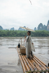 Woman in Hanfu attire holds an umbrella while standing on a bamboo raft in Xingping, China