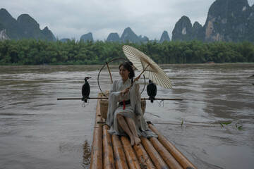 Hanfu girl with umbrella on bamboo raft in Xingping posing with cormorants