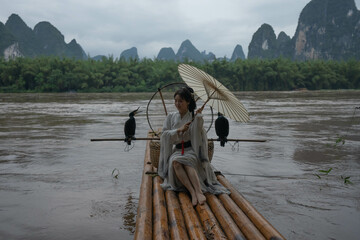 Hanfu girl with umbrella on bamboo raft in Xingping posing with cormorants