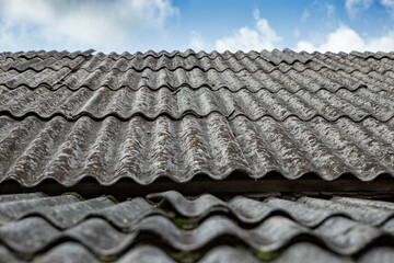 Gray asbestos sheets on a house rooof, pespective view with blue sky and white clouds