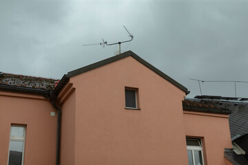 A tall building featuring a prominent roof antenna situated on top of it, reaching towards the sky amidst clouds and nearby trees