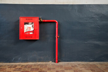 Fire hose in red box. Pipe roll for fire emergency in red metal cabinet on gray painted concrete wall with tiled floor as part of firefighting system of industrial production plant with copyspace.