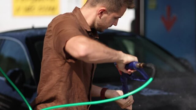 Handsome man washes his luxury car at a self-service car wash. Water under pressure