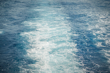 Wake of a ship creating frothy, white trails on the blue ocean surface.