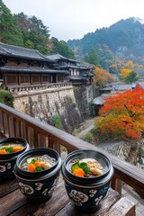 Fototapeta premium Platos tradicionales japoneses de sopa caliente con verduras, servidos en un balcón con una vista panorámica de un paisaje otoñal.