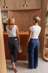Two women in jeans, photographed from behind, are waiting at the reception