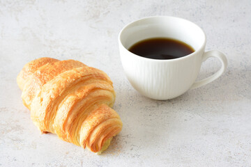 a cup of coffee next to a french croissant close up  