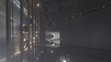 Vertical video of cars passing on the Brooklyn Bridge in New York, USA, filmed on a dark, cold, and foggy night, with the city's skyscrapers in the background. - Powered by Adobe