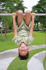 Portrait of Asian boy child hanging upside down on equipment at playground in garden. © zilvergolf