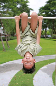 Portrait of Asian boy child hanging upside down on equipment at playground in garden.