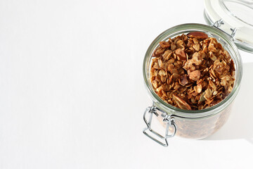Storing Homemade Granola in Reusable Glass Jar. Glass Container with Oat Granola on White Kitchen Table.
