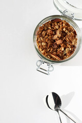 Open Glass Storage Jar with Granola on White Kitchen Table. Breakfast Preparing.