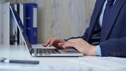 Businessman with blue suit is working on his laptop, typing on the keyboard in the office. Business concept