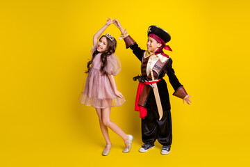 Full size photo of two little kids hold hands dance halloween pirate princess costume isolated on yellow color background © deagreez