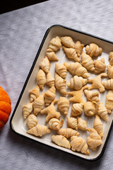 Small croissants and cookies in the shape of cats from puff pastry in a white baking dish, next to a pumpkin