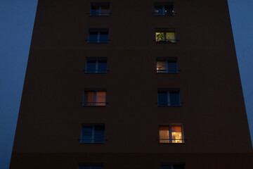 A tall building featuring numerous windows that are illuminated at night, creating a vibrant and...