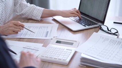 Female bookkeeper is working on finances papers with a colleague, using magnificent glass, calculator and laptop. Audit, taxes