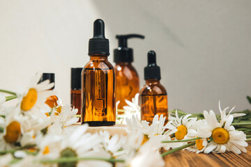 Set of natural cosmetics. Amber bottles with facial, bath liquid on a wooden table with white field chamomile. Front view