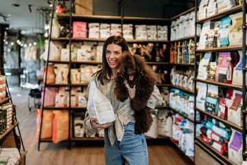 Beautiful young woman enjoying in modern pet shop together with her adorable brown toy poodle.