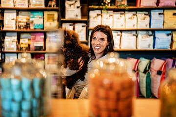 Beautiful young woman enjoying in modern pet shop together with her adorable brown toy poodle.