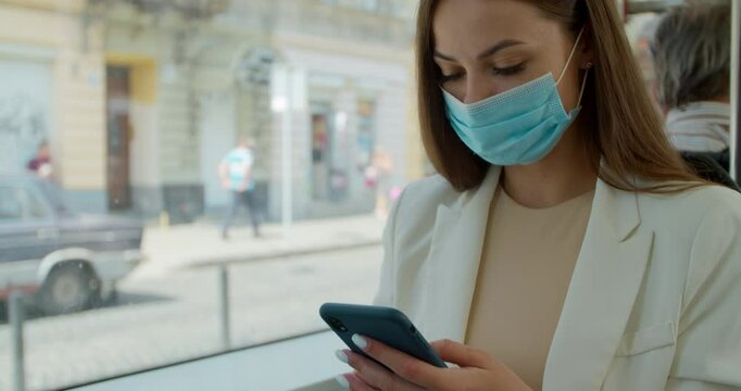 Coronavirus pandemic is over, quarantine end, young woman in protective medical face mask in a public transport using smartphone. Young girl usig app on a smartphone.