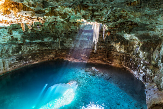 Man swimming in the blue water of a cenote with sunlight from the top, Yucatan, Mexico