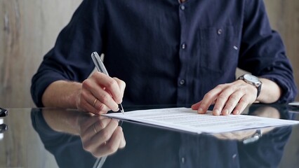 Businessman in dark blue t-shirt is signing contract at desk. Close-up of a male executive signing...