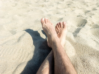 man feet sitting on hot sand over the sea. Holiday concept. man feet relaxing on beach, enjoying sun and splendid view. barefoot sunbathing on summer beach. Happy on holidays vacation concept.