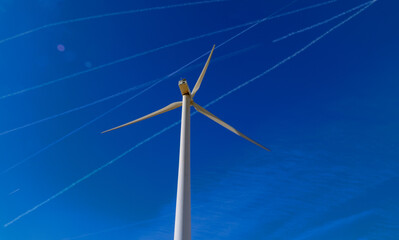 Fototapeta premium Wind turbine against a blue sky with jet trails.