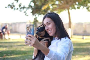 Smiling woman taking a selfie with her pinscher dog in a sunny park