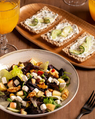 A fresh salad with feta, walnuts, apples, and toasts with cucumber and tsasiki, accompanied by orange juice, healthy breakfast