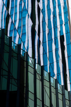 A modern skyscraper facade reflecting blue and white hues in wavy patterns, creating an abstract and dynamic visual impression of urban architecture.