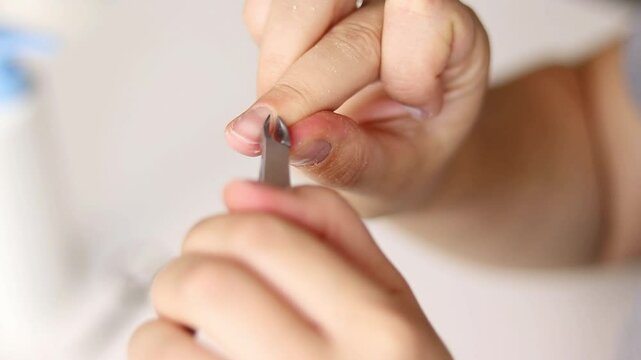 Close up of woman removing cuticles from fingers with tweezers, natural manicure 