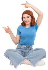 Obraz premium Full body view red bob hair caucasian 20s woman sit floor wear jeans and blue t shirt toothy smile pointing aside copy space with two finger demonstrating, recommending advertisement concept idea.