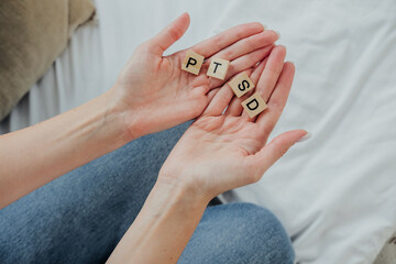 Hands holding wooden tiles spelling PTSD, symbolizing mental health awareness and discussion