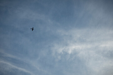 A small plane soars gracefully through a vast expanse of blue sky, dotted with fluffy white clouds.