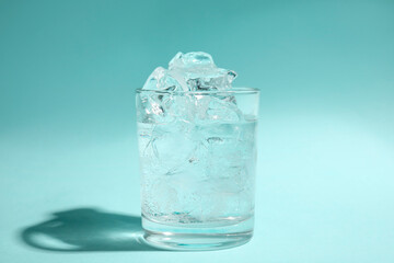 Refreshing water with ice in glass on turquoise background
