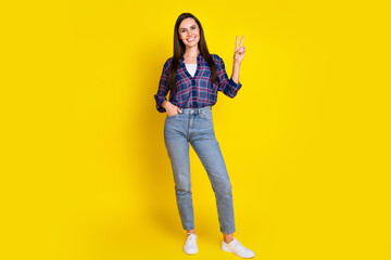 Full body photo of pretty young girl show v-sign wear trendy plaid outfit isolated on yellow color background