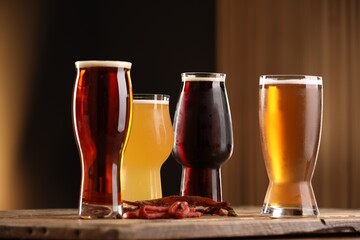 Glasses with different types of beer and snacks on wooden table against color background