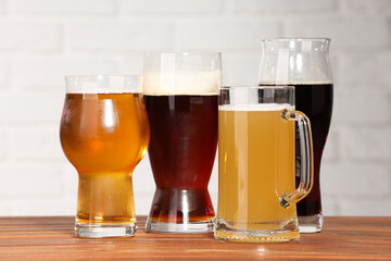 Glasses with different types of beer on wooden table against white brick wall, closeup