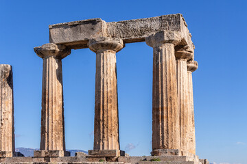 Fototapeta premium Corinth Temple of Apollo, Ancient ruins with weathered stone columns under a clear blue sky, Greek classical architecture. Corinth, Greece