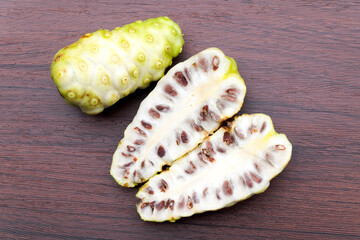 Noni or Morinda or Morinda citrifolia or Indian mulberry fruits, whole and cut lengthwise isolated on dark wooden background top view. flat lay.