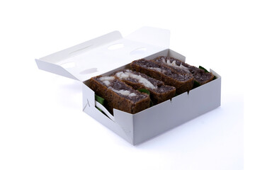 Black glutinous rice flour Thai coconut pancake in paper box isolated on white background with clipping path closed up stack. Kanom Ba Bin in Thai.