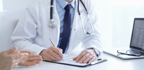 A doctor and a patient. The physician, wearing a white medical coat over a blue shirt and tie, is...
