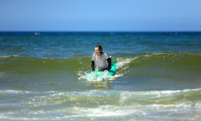 Surfer. Teenage girl learning to surf on foam in the ocean. First surfing lesson. Amateur surfer. Surfing training. Photo for surfing school advertising on social media.